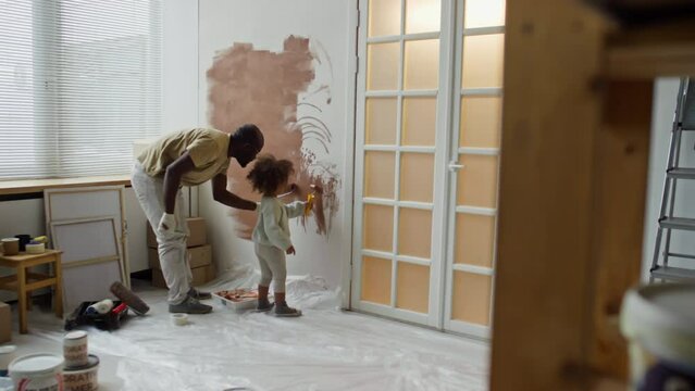 Back full footage of single dad remodeling room into nursery while painting walls brown with his little daughter