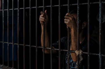hands of a prisoner behind prison bars
