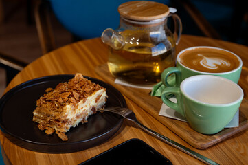 a cup of coffee and a cup of green tea and cake on a wooden table in a cafe.