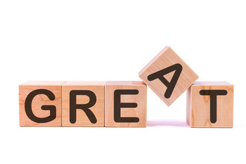Word GREAT is made of wooden building blocks lying on the table and on a light background.