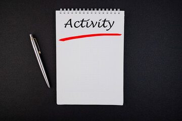 The text, the word Activity, is written in a notebook lying on a black table with a pen. Business concept