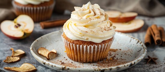 Apple cupcake topped with cream cheese frosting, garnished with dried apple slices and a sprinkle of cinnamon powder. 