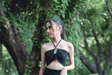 Young woman in goth-inspired attire posing pensively in a lush forest backdrop