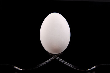 egg is balanced on forks with a dark background. Minimalism.