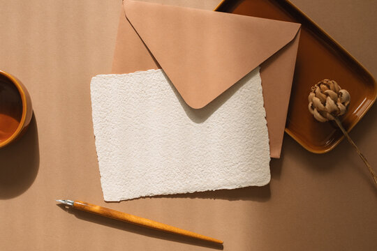 Overhead view of blank piece of homemade deckle edge card, an envelope,  calligraphy pen and flower on a wooden table