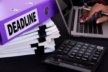 Text, word DeadLine is written on a folder lying on documents on an office desk with a laptop and a...