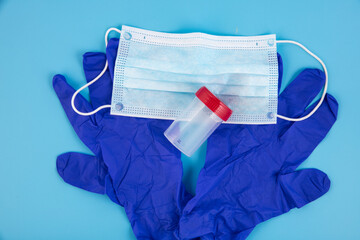 Blue disposable medical, surgical gloves, medical mask and test flask on a blue background. Medical...