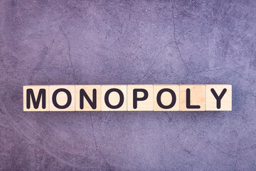 Monopoly written on a wooden cube on a grey background.