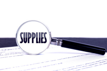 Magnifying glass with text concept word SUPPLIES on a dark table and a light background.