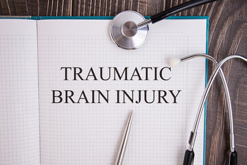 Notebook page with text TRAUMATIC BRAIN INJURY, on a table with a stethoscope and pen, medical...