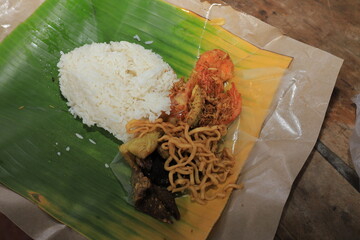 Nasi Bungkus, a typical Indonesian food served with oil paper filled with rice, fresh vegetables, chicken, and hot chili sauce.