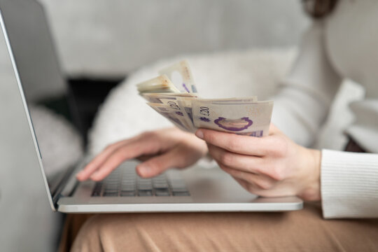 Close-up of a woman holding a handful of cash while using a computer
