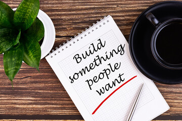 Build something people want notepad writing concept on a wooden background with pen and cup of...