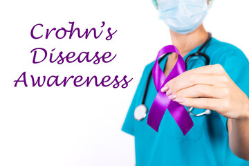 Female doctor in blue uniform with purple awareness of ribbon in hand for Crohn's Disease