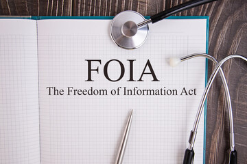Notebook page with text FOIA The Freedom of Information Act, on a table with a stethoscope and pen,...