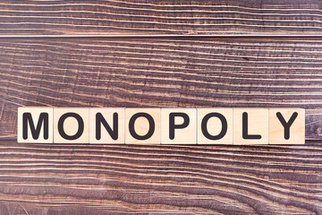 Monopoly written on a wooden cube on a wooden background.
