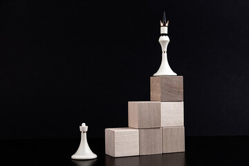 Chess figures on a toy wooden ladder - a chess pawn on the bottom and a chess queen on top, concept...