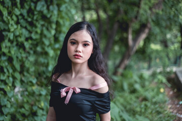 Fototapeta premium Young woman in goth-style dress posing in lush forest, capturing mystical and enchanting vibes