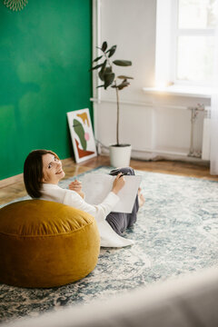 Brunette girl  in white 
jacket reading book and smil in room with green wall