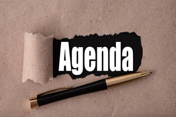 AGENDA text written under torn paper and a recumbent metal pen. Business strategy concepts.