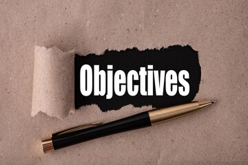 OBJECTIVES text written under torn paper and a recumbent metal pen. Business strategy concepts.