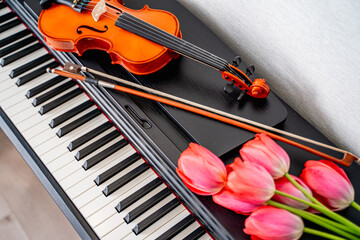 an elegant violin, a bow and a bouquet of red tulips with delicate petals lie on the piano, a...
