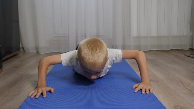 A little athletic boy trains at home, he does push-ups from the floor. Training at home during quarantine. 