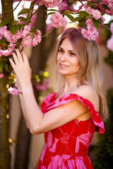 Naklejka premium portrait of a blonde woman next to a blooming Japanese cherry tree on a spring day.
