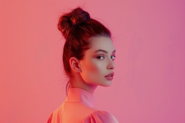 An alluring portrait of a beautiful young woman with a big bun hairstyle against pink light background, giving a gaze over shoulder. Copy space.