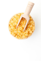 Shell shaped pasta in bowl with wooden scoop on white background. Top view. Space for a text