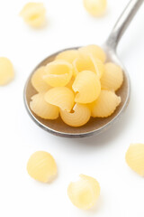 Yellow, small shell shaped pasta in iron spoon on white background. Close-up