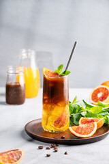 Coffee with orange juice (bumble) in a tall glass with ice and mint on a wooden plate on a blue background