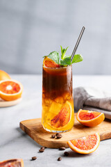 Coffee with orange juice (bumble) in a tall glass with ice and mint on a wooden board on a light background with coffee beans, fruits and morning shadows.