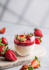 Strawberry and cream panna cotta in glass with fresh berries on a marble board on a light...