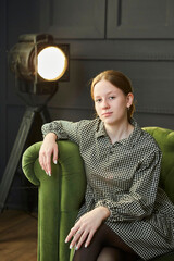 A beautiful young girl is sitting on a sofa in the studio in the spotlight. Stylish loft interior. - 788033333