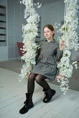 Portrait of a beautiful young girl sitting on a swing in a photo studio. Floral light interior - 788033355