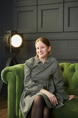 A beautiful young girl is sitting on a sofa in the studio in the spotlight. Stylish loft interior. - 788033363