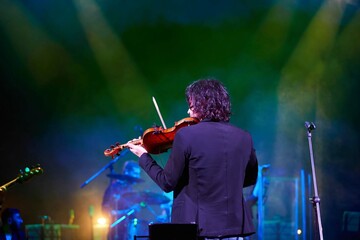 A violinist musician stands on stage with a violin in his hands during a concert. There is a bright light from the floodlights around. - 788035548