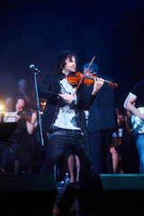 A violinist musician stands on stage with a violin in his hands during a concert. There is a bright light from the floodlights around. - 788035575