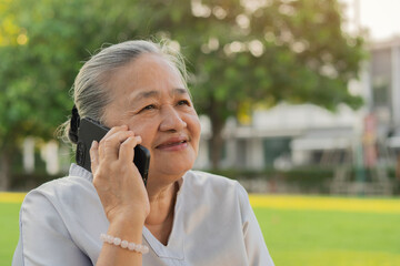 Cheerful old Asian woman excited on receiving some good news over smartphone at park.