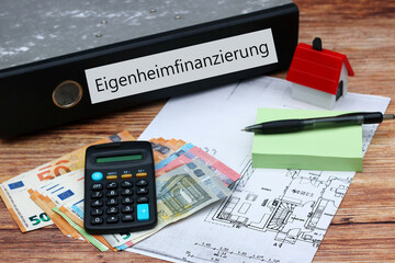 Ordner mit der Aufschrift "Eigenheimfinanzierung" mit Taschenrechner und Euro-Banknoten.
