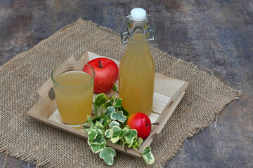 Naturally cloudy apple juice in a bottle and glass decorated with apples.