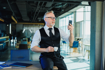 Cute gray-haired man sitting and talking on the phone in a relaxed office workplace. The manager in the office works online