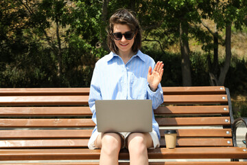 The girl works on a laptop while sitting on a bench