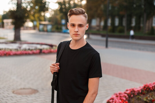 handsome youth fashionable man with a hairstyle in a black mock-up T-shirt with a backpack walks in the city