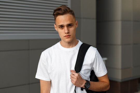 Handsome fashion young guy model tourist with hairstyle in a white T-shirt with a backpack in the city