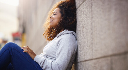 Happy, relax and black woman by wall in city, urban town and street or lens flare by building in Houston, Texas. Earphones, student and gen z girl with smile for freedom, calm or listening to music