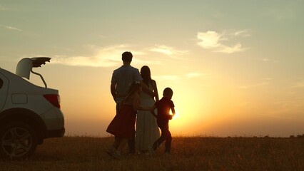 Parents children at sunset by car in field. Happy man woman hugging embracing girl boy kids running...