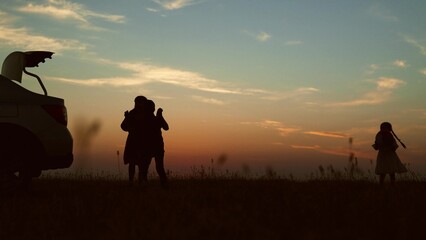 Silhouettes of children playing at sunset by car. Cute cheerful funny kids children siblings...