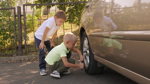 Two little brothers help Dad fix the car, they unscrew the bolts on the wheel with a torque wrench. Children play and imagine themselves as car mechanics. 